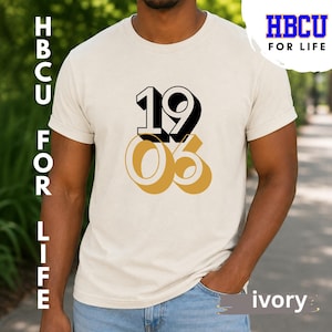 Może przedstawiać: T-shirt z krótkim rękawem w kolorze kości słoniowej z nadrukowaną na piersi liczbą 1906. Liczba 19 jest czarna z cieniem, a liczba 06 jest złota z cieniem. Koszulka ma okrągły dekolt i standardowy krój.