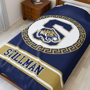 May include: A navy blue fleece blanket with a gold and white circular design featuring a tiger head and the letter "S". The words "Stillman" are printed in gold on the blanket.