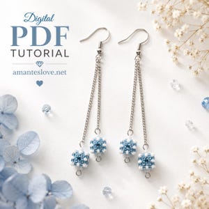 May include: A pair of dangle earrings featuring silver-tone chains and small, square, beaded cubes in shades of blue and white. The text Digital PDF TUTORIAL amanteslove.net is visible. The earrings hang from silver-tone metal hooks.