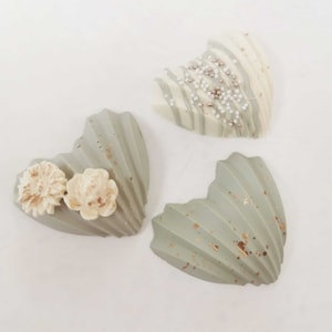 Può includere: Tre cioccolatini a forma di cuore, uno bianco con codette argentate e due verdi con accenti dorati. Un cioccolatino verde è decorato con fiori bianchi.