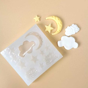 Puede incluir: Un molde de silicona blanco con múltiples formas de estrellas, nubes y medias lunas. También hay varias piezas de resina terminadas en forma de estrellas, nubes y media luna.