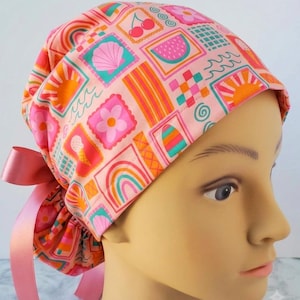 May include: A scrub cap featuring a repeating pattern of summer-themed icons including cherries, watermelon slices, rainbows, seashells, flowers, and ice cream cones in shades of pink, orange, and teal, finished with a pink satin ribbon tie.