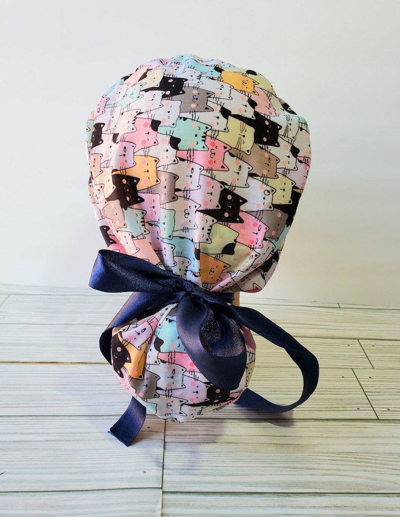 Puede incluir: Un gorro quir&uacute;rgico con un dise&ntilde;o de estampado de gatos coloridos. El gorro est&aacute; atado con una cinta azul marino.