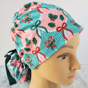 May include: A pink and teal scrub cap with a Christmas-themed pattern. The cap features candy canes, bows, and holly leaves. The cap has a dark green tie in the back.