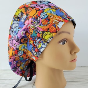 May include: A colorful surgical scrub hat with a pattern of cartoon characters, including Smurfs, Care Bears, and My Little Pony. The hat has black ties and is made of a soft, comfortable fabric.
