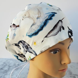 May include: White scrub cap with a watercolour design of arctic animals, including a polar bear, narwhal, and orca. The cap has a drawstring closure and is designed for medical professionals or those in healthcare.