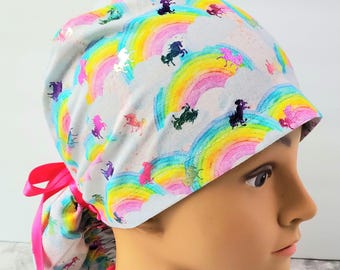 May include: A surgical scrub hat with a tie, featuring a white background with a colorful rainbow and unicorn pattern.