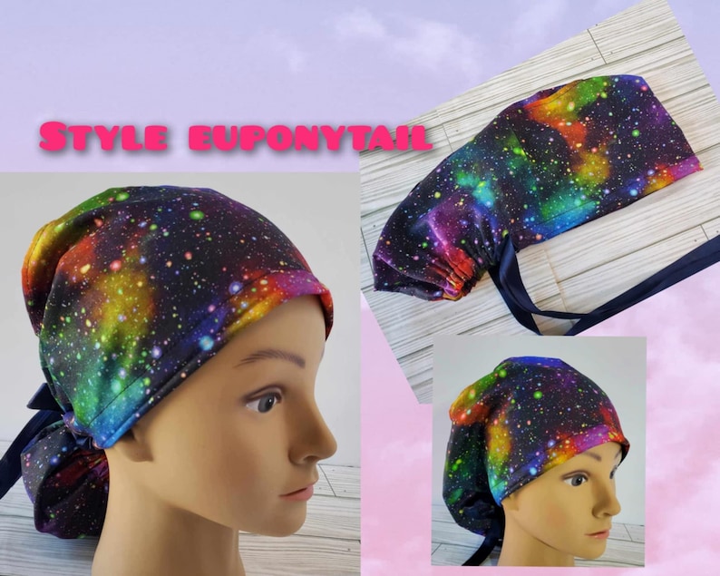 May include: A colorful galaxy print surgical scrub hat with a ponytail opening. The hat is tied with a navy blue ribbon.  The hat is shown on a model with a ponytail.