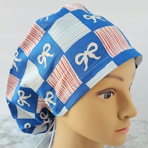 May include: A blue and white patterned scrub cap with a bow design. The cap features a checkered pattern with white bows and red and white striped accents. The cap is tied at the back with white ties.