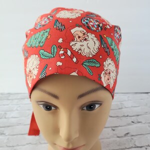 May include: Red scrub hat with a Christmas print featuring Santa Claus, candy canes, Christmas trees, and ornaments.