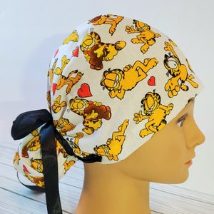 May include: White surgical scrub hat with a black tie. The hat features a repeating pattern of Garfield cartoon characters with red hearts.