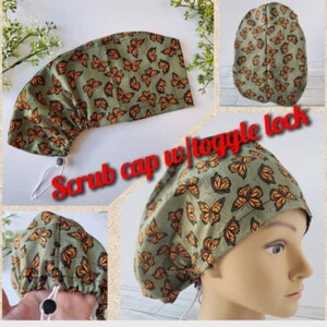 May include: Green scrub cap with a butterfly print and a toggle lock. The cap is made of fabric and has a drawstring.