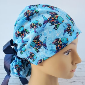 May include: Blue surgical scrub hat with a colorful fish pattern and white bubbles. The hat has a navy blue ribbon tie.
