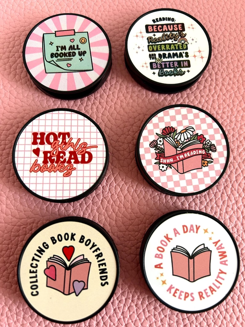 Pode incluir: Uma cole&ccedil;&atilde;o de acess&oacute;rios redondos, pretos e brancos com v&aacute;rios designs com tema de livros. Os designs incluem frases como "Estou toda reservada", "Garotas quentes leem livros" e "Um livro por dia mant&eacute;m a realidade longe". Os acess&oacute;rios t&ecirc;m um esquema de cores rosa e branco.