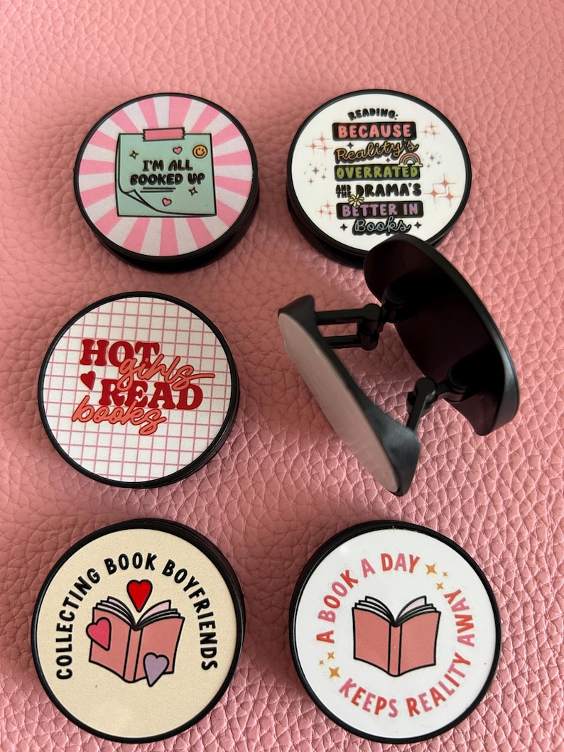 Pode incluir: Uma cole&ccedil;&atilde;o de suportes redondos para telem&oacute;vel com v&aacute;rios designs com tema de livros. Um diz "I'M ALL BOOKED UP", outro diz "READING: BECAUSE Reality's OVERRATED, DRAMA'S BETTER IN Books+". Outros suportes dizem "HOT girls READ books", "COLLECTING BOOK BOYFRIENDS" e "A BOOK A DAY KEEPS REALITY AWAY".