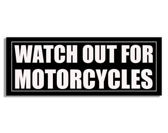 Può includere: Un cartello rettangolare nero con testo bianco che recita "WATCH OUT FOR MOTORCYCLES". Il testo è in grassetto, senza grazie e centrato. Il cartello ha un bordo bianco.