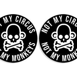Op de afbeelding: Twee ronde stickers in zwart en wit met de tekst "Not My Circus Not My Monkeys" en een schedel met gekruiste beenderen en apenoren.
