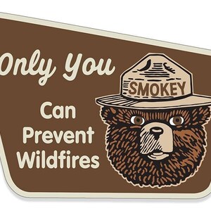 May include: A brown and beige sign with a cartoon bear wearing a ranger hat that says "Smokey" on it. The sign says "Only you can prevent wildfires".