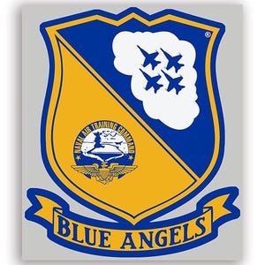 Può includere: Un emblema a forma di scudo con un design blu e oro. La metà superiore è blu con quattro jet bianchi in formazione. La metà inferiore è dorata con un emblema circolare e la scritta "BLUE ANGELS" su uno stendardo.
