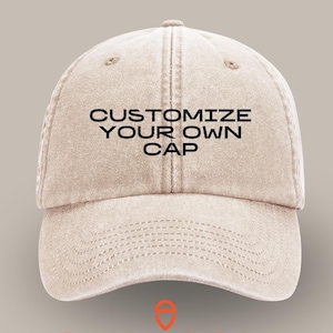 Può includere: Un cappello da baseball in cotone beige con il testo "CUSTOMIZE YOUR OWN CAP" in lettere nere. Il cappello è mostrato frontalmente, con il visore rivolto verso il basso. Il nome del marchio "vincent daimon" è stampato in arancione sotto il cappello.