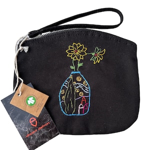 Könnte beinhalten: Schwarze Canvas-Zipper-Tasche mit einem bunten gestickten Design einer Vase mit Blumen. Die Tasche hat einen schwarzen Riemen und ein Etikett mit der Aufschrift "Global Organic Textile Standard GOTS Certified".