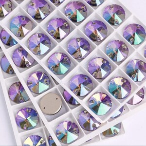 May include: Close-up of iridescent, round rhinestones in a white plastic tray. The rhinestones have a flat back and are arranged in a grid pattern. The colors shift from purple to blue and green, reflecting light.