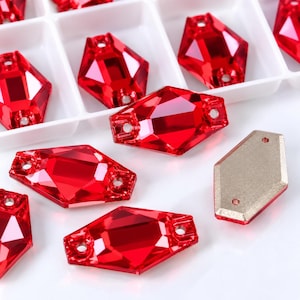 May include: A collection of faceted, diamond-shaped red crystals with two holes for sewing. Each crystal features a brilliant, reflective surface and a flat, metallic-toned backing. The items are arranged both inside a white plastic organizer tray.