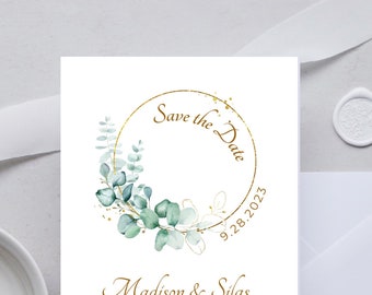 Può includere: Carta di salvataggio della data con un cerchio dorato e foglie di eucalipto verdi. Il testo recita "Save the Date" con la data "9.28.2023" sotto. I nomi "Madison & Silas" sono scritti in corsivo sotto il cerchio. L'indirizzo "123 ANYWHERE ST ANY CITY, ST 12345" è stampato sotto i nomi. Il testo "formal invitation to follow" è scritto in corsivo sotto l'indirizzo.