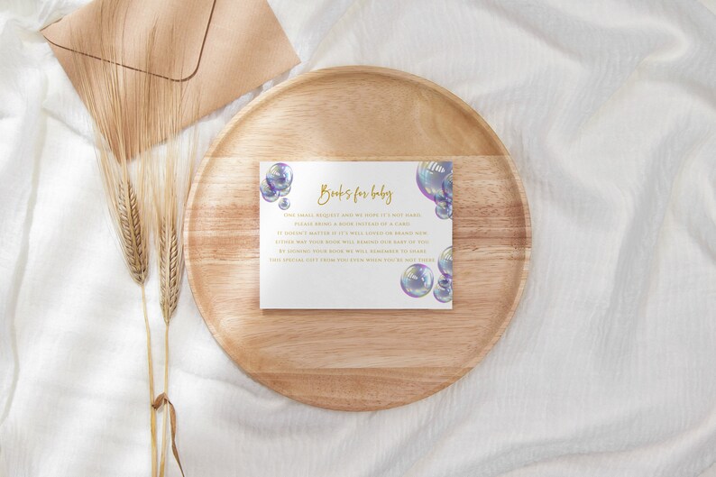 May include: A white card with gold text that reads "Books for Baby". The card is decorated with iridescent blue and purple bubbles. The text on the card reads: "One small request we have for you, it's most basic. Please bring a book instead of a gift. It doesn't matter if it's well-loved or brand new, either way your book will become our baby's too. By bringing a book, you will be helping our baby to grow. This special gift from you will be remembered for years."