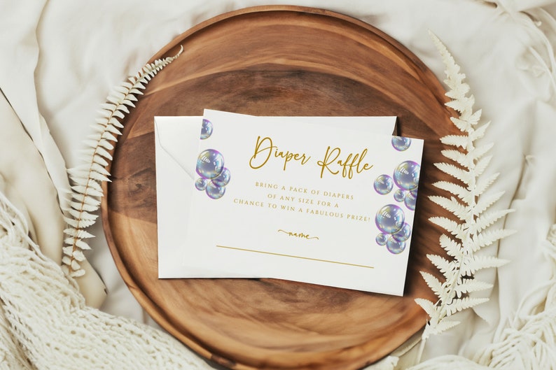May include: White card with gold text that reads "Diaper Raffle" and "Bring a pack of diapers of any size for a chance to win a fabulous prize!" The card is decorated with iridescent blue and purple bubbles.