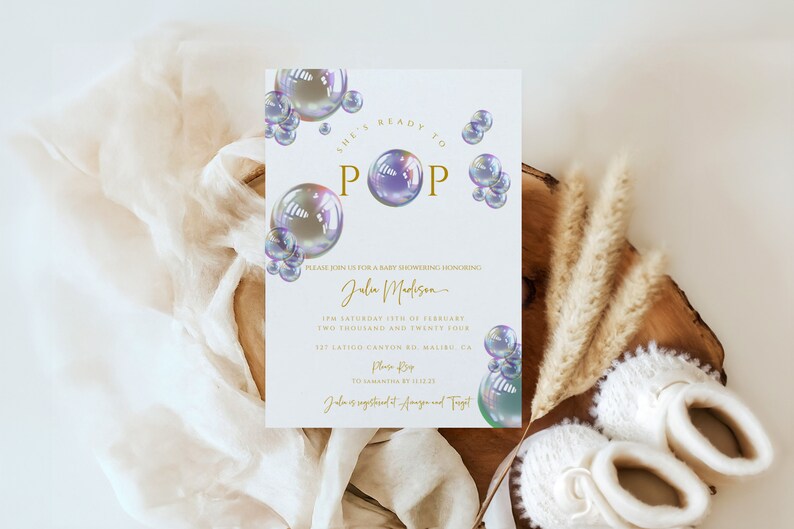May include: A white baby shower invitation with gold and white text overlay. The text reads "She's ready to pop" with a large iridescent bubble graphic. The invitation includes the name "Julia Madison" and the date and time of the event.