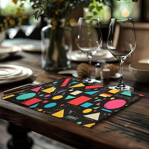 May include: A rectangular print featuring a black background covered in a variety of colorful geometric shapes including circles, triangles, and rectangles in shades of yellow, red, pink, and blue, accented by small white dots and thin lines.
