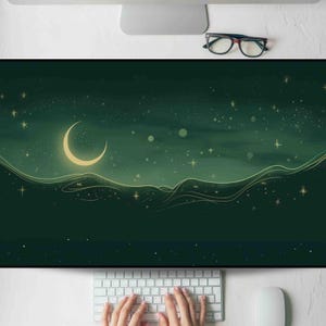 May include: A green and gold desk mat featuring a crescent moon and stars design. The mat has a dark green background with a stylized landscape and celestial elements. A keyboard and mouse are visible in the foreground.