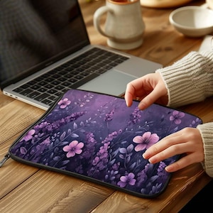 May include: A rectangular laptop sleeve featuring a dark purple background with a repeating pattern of light purple and pink flowers, slender stems, and small leaves. The sleeve has a black zipper closure along the top edge and sides.