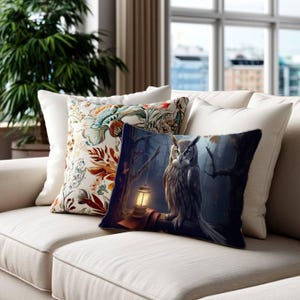 May include: A rectangular throw pillow featuring a dark, atmospheric forest scene with a detailed owl perched next to a glowing lantern. Beside it sits a square throw pillow with a cream background and a vibrant, multi-colored floral pattern.
