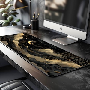 May include: A rectangular desk mat featuring a celestial design with black, gold, and white clouds, a crescent moon, and gold lines. The mat is placed on a dark desk, with a computer monitor and desk accessories in the background.