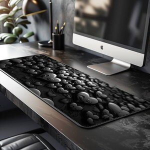 May include: Black mouse pad with a 3D heart pattern. The pad is rectangular and sits on a dark desk. The hearts are raised and create a textured surface. A computer monitor and desk accessories are in the background.