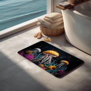 May include: A rectangular bath mat featuring a dark underwater scene with three glowing jellyfish in shades of orange, white, and blue, surrounded by vibrant purple and yellow coral reefs against a deep black background with small bubbles.