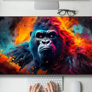 May include: A vibrant, colorful mousepad featuring a gorilla with a stern expression. The gorilla is depicted with a mix of blue, red, and orange hues, set against a dynamic, abstract background. The mousepad is rectangular and sits on a white desk, with a keyboard and mouse visible.