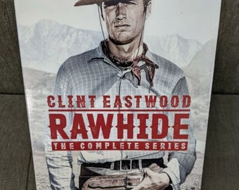 May include: A DVD box set featuring Clint Eastwood in the TV series "Rawhide". The box set features a photo of Clint Eastwood in a cowboy hat and a brown leather vest. The text "Clint Eastwood Rawhide The Complete Series" is printed on the box.