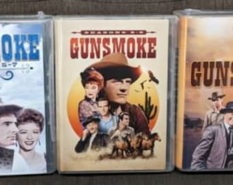 May include: Three DVD cases with Gunsmoke on the front. The first case is for seasons 5-7, the second case is for seasons 1-3, and the third case is for seasons 10-12. The cases are all black with a white border and the Gunsmoke logo in the center.
