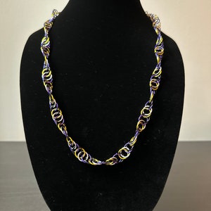 May include: A purple, gold, and silver chain necklace on a black display stand.