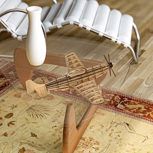 May include: A wooden model airplane sits on a glass coffee table with a wooden base. The table is on a rug with a floral pattern. A white vase sits on the table.