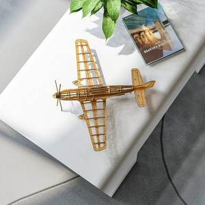May include: A wooden model airplane on a white surface with a book titled "Travel Guide" on top of the surface.