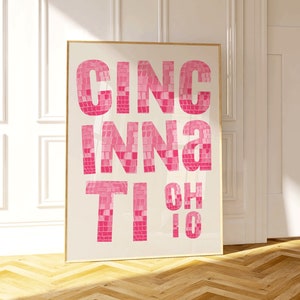 Puede incluir: Una impresión enmarcada con las palabras "Cincinnati, OH" en azulejos de mosaico rosa sobre un fondo blanco.
