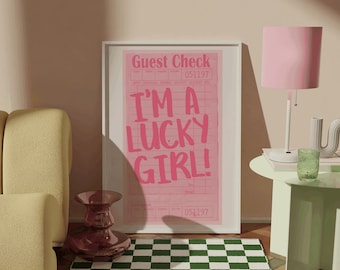 May include: A framed print with the text "I'm a lucky girl!" on a pink and white guest check. The print is hanging on a wall with a green and white chequered rug in front of it. There is a pink lamp with a white base and a green glass on a light green side table.