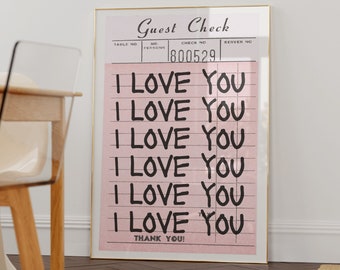 May include: A framed pink print with the words "I LOVE YOU" repeated multiple times in black, resembling a guest check. The print also includes the words "Guest Check" and "THANK YOU!" in black. The frame is gold.