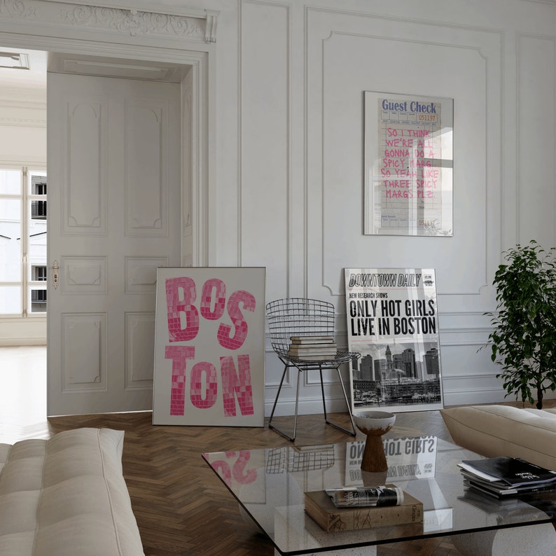May include: A white room with a white couch, a glass coffee table, a metal chair, and three posters on the wall. The posters are a pink and white "Boston" poster, a black and white poster with the text "Only Hot Girls Live in Boston", and a black and white poster with the text "Guest Check".