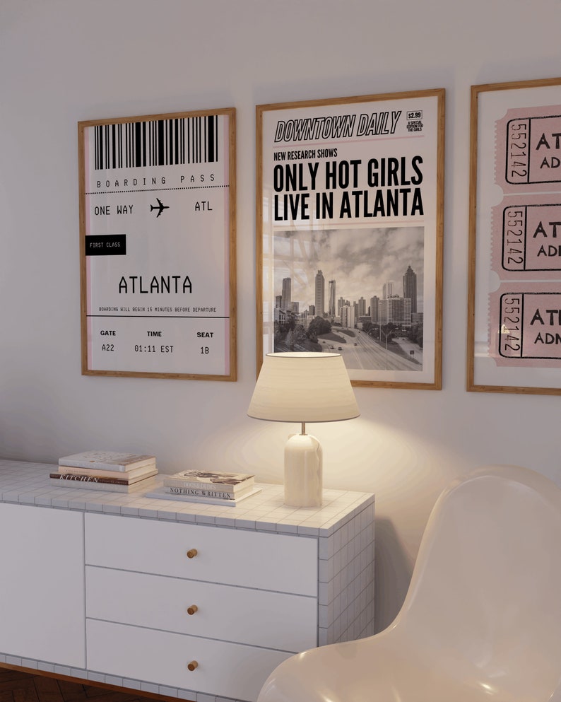 May include: A framed print featuring a black and white image of a boarding pass for a flight to Atlanta. The print is hanging on a white wall alongside a framed print of a newspaper article with the headline "Only Hot Girls Live in Atlanta".