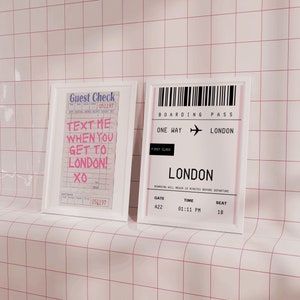 May include: Two framed prints on a white tiled wall. The left print is a white frame with a pink and white guest check that says "Text me when you get to London! XO". The right print is a white frame with a black and white boarding pass that says "Boarding Pass One Way London First Class London Gate A22 Time 01:11 PM Seat 18".